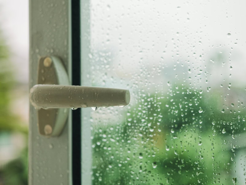 A Guide to Indoor Humidity Control. Raindrop on window with Handle Blur tree background Rainy Season.